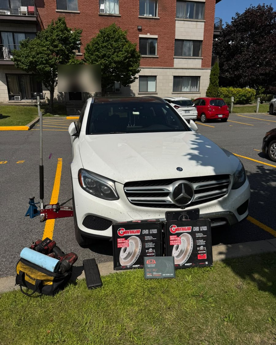 Un Mercedes-Benz GLC blanc dans un stationnement, ses disques Genius et plaquettes neufs posés devant, prêts à être installés.